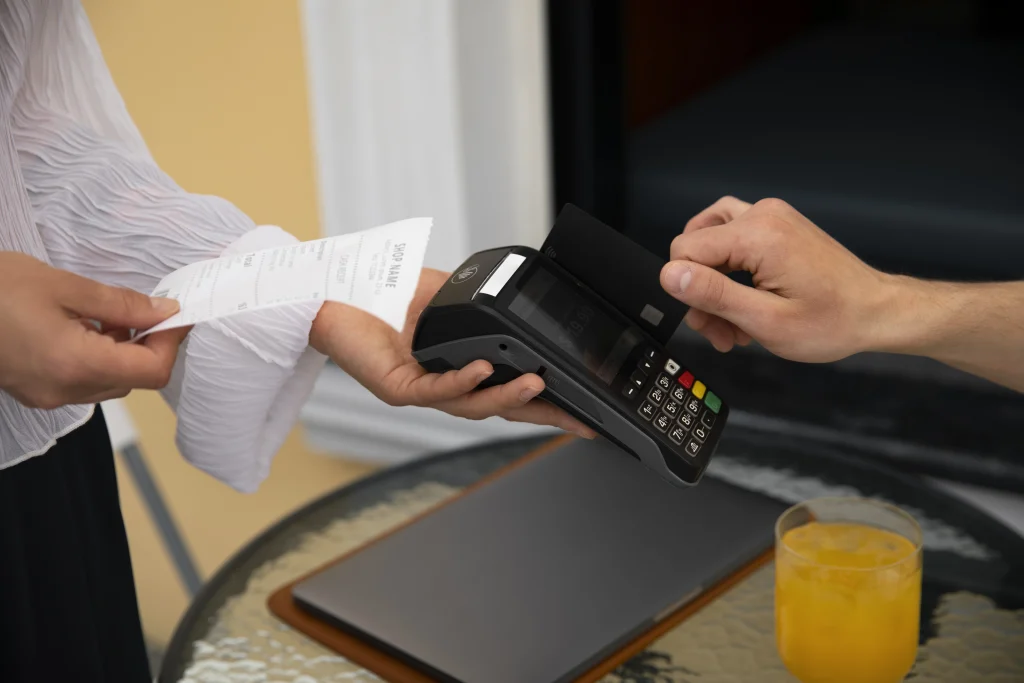 A staff member holding a receipt while a customer inserts a credit card into a terminal, providing essential POS reporting for sales to track daily revenue.