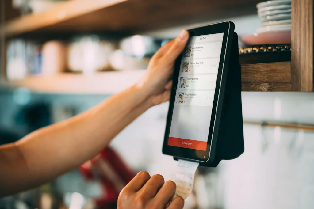 A worker using a modern touchscreen POS terminal to process a food order and print a receipt, showcasing the best POS for small business efficiency.